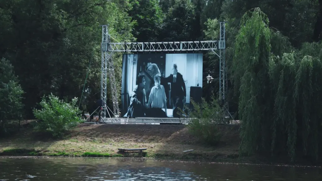 Didelis ekranas rodo filmą parke šalia vandens telkinio rudens sezono metu.