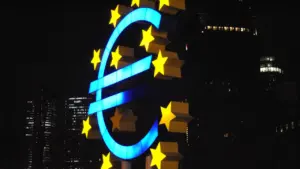 Šviečiantis Europos centrinio banko simbolis naktiniame miesto fone, simbolizuojantis euro zonos finansų politiką.
