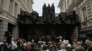 Žmonės susirinkę Vilniaus dramos teatro kiemelyje po garsiąja „Mūzų“ skulptūra stebi kultūrinį renginį.
