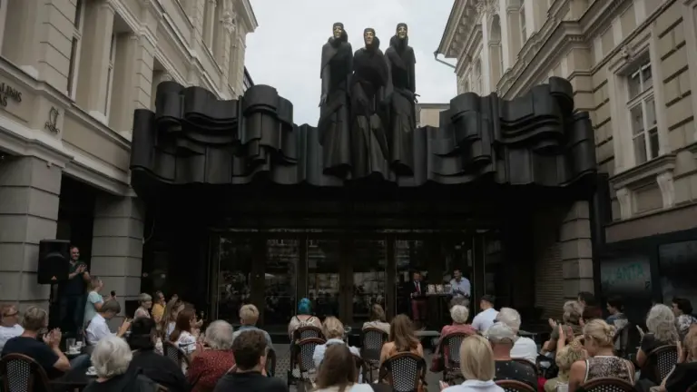 Žmonės susirinkę Vilniaus dramos teatro kiemelyje po garsiąja „Mūzų“ skulptūra stebi kultūrinį renginį.