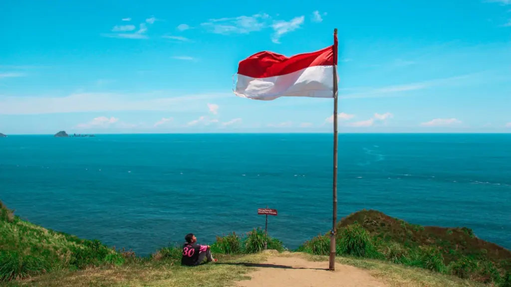 Indonezijos vėliava plevėsuoja pajūryje, simbolizuojanti šalies laisvę ir nepriklausomybę nuo kolonizatorių.