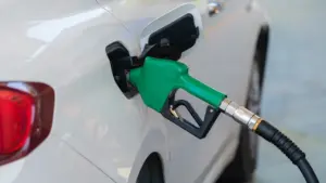 Balto automobilio kuro bakas pildomas degalais degalinėje, aiškiai matomas pistoletas.