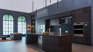 Moderni tamsi LG Signature virtuvė su sala ir dideliais arkiniais langais šviesioje erdvėje.