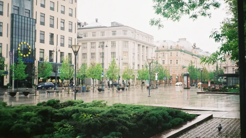 Šlapias Vilniaus miesto centras lietingą dieną su pastatais ir žaliuojančiais medžiais.