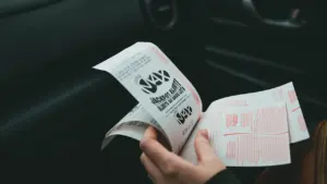 Žmogaus rankose laikomas loterijos bilietas sėdint automobilyje po sėkmingo laimėjimo.