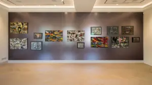 Daugybė spalvingų abstrakčių paveikslų pakabintų ant tamsios sienos šiuolaikinėje meno galerijos erdvėje.